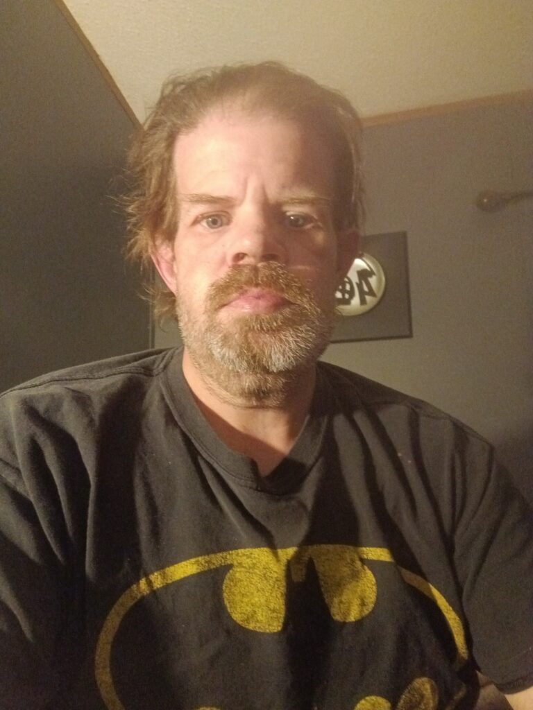 Front-facing photo of white male with a shirt with a Batman logo. 