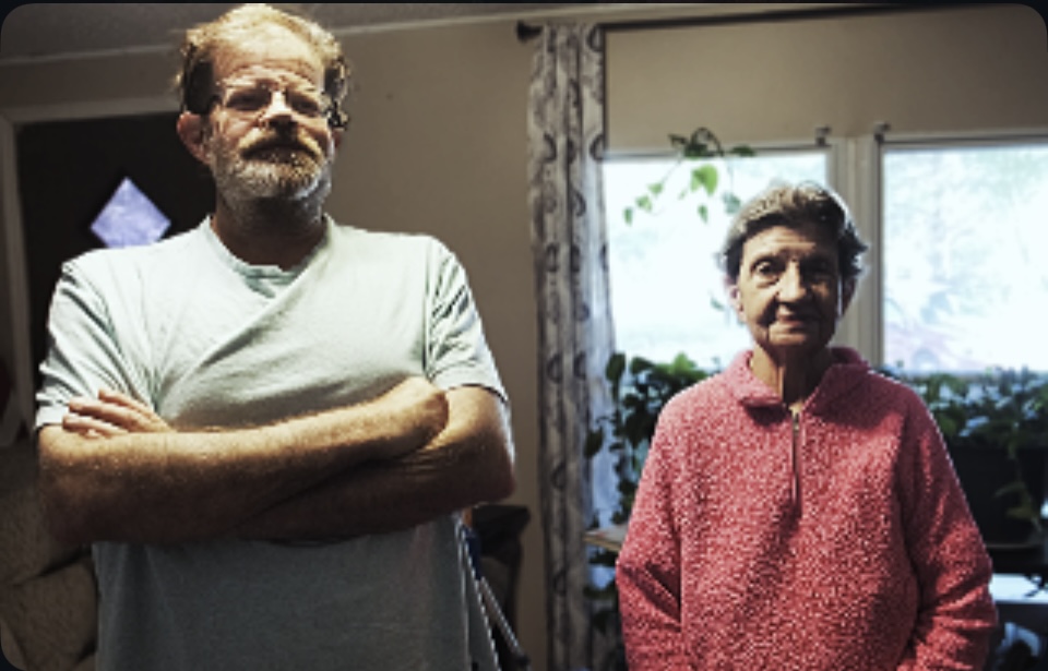 A tall man with arms crossed stands next to a woman who is a couple feet shorter. 